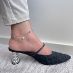 Load image into Gallery viewer, A foot wearing a black heel with a gold anklet featuring a blue evil eye charm and a heart-shaped charm.