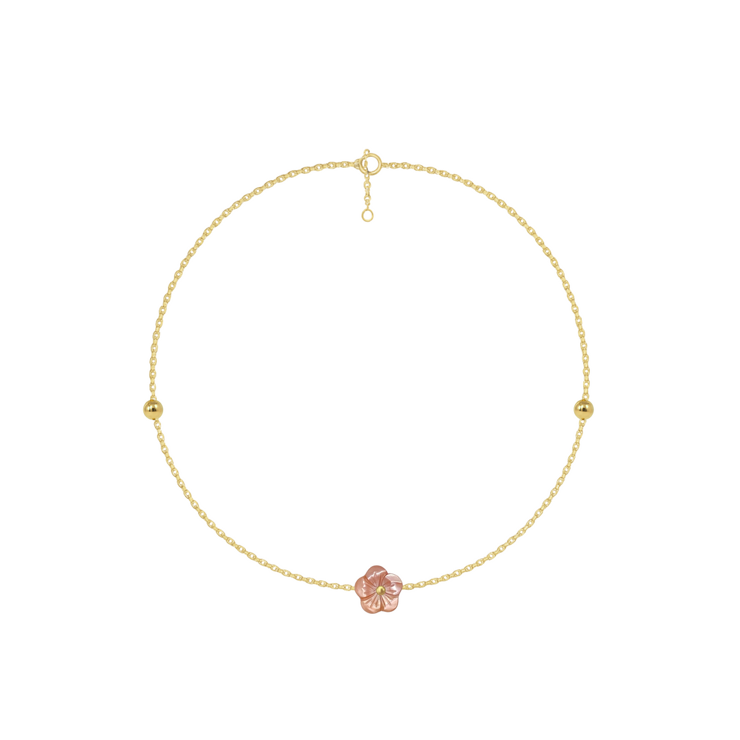 Gold anklet with a pink flower charm on a white background